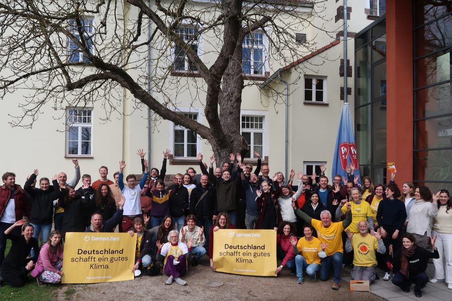 Hier sind Menschen aller Altersgruppen zu sehen, die die Arme jubelnd hochhalten. Sie halten gelbe Banner nach vorne auf denen drauf steht: Deutschland schafft ein gutes Klima!
